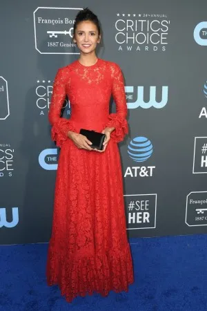 Nina Dobrev in a red lace long gown with long sleeves attends the Critics Choice Awards red carpet 2019