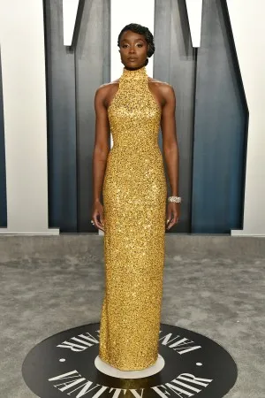 Kiki Layne in a gold sequin sparkly gown with high neckline and slit at the back attend the 2020 Vanity Fair Oscar party